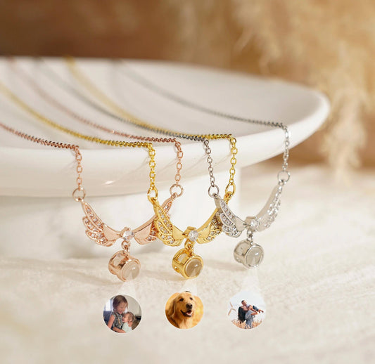 May include: Three silver, gold, and rose gold angel wing necklaces with a small round pendant that displays a projected image. The pendants are filled with clear crystals. The image projected from the pendants are of a young girl, a golden retriever, and a couple.